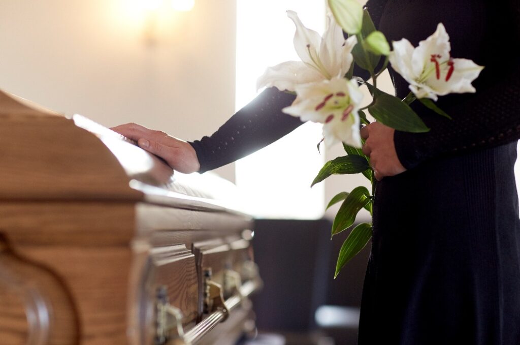 Frau mit Lilienblüten und Sarg bei Beerdigung